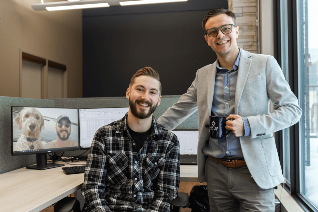 Two men smiling at camera with workstation behind - Virtus Group LLP