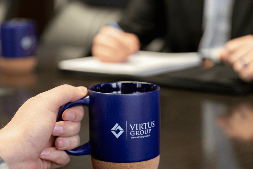 Man holding blue Virtus Group Mug at conference table with colleague writing on notepad in background