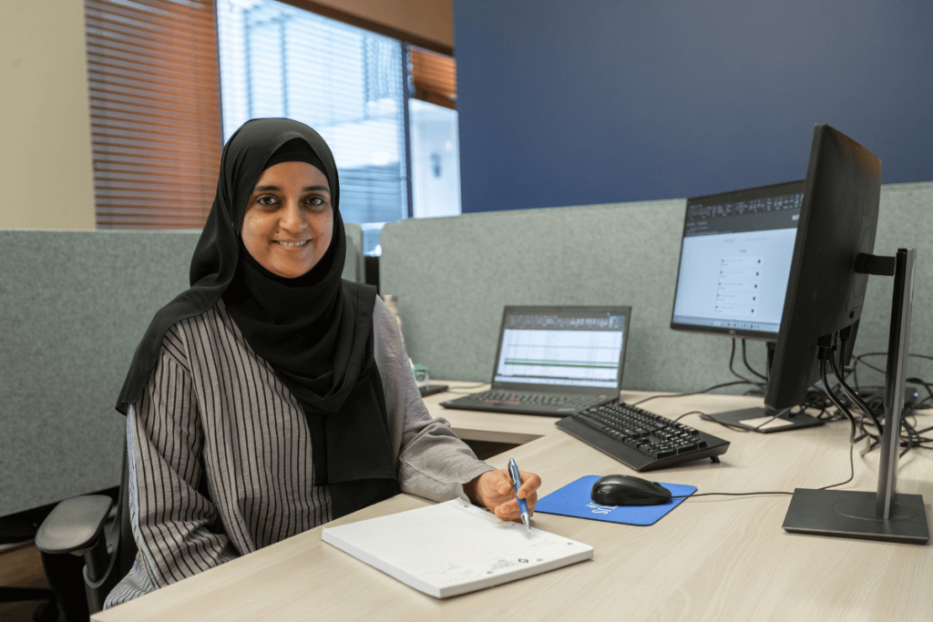 Woman in hijab sitting at her desk smiling at camera