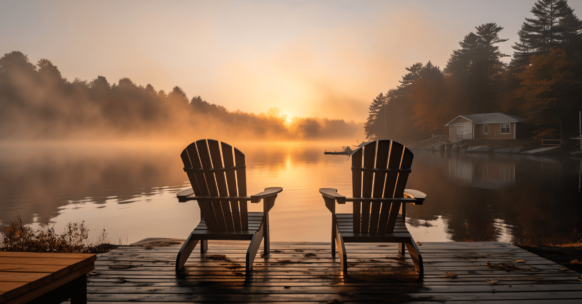 Lake life with two Muskoka chairs on a dock at a misty lake at sunrise.