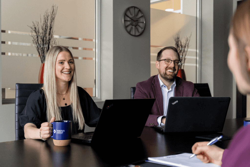 Blonde haired woman and brown haired man with a beard and glasses sitting in accounting firm board room with black laptops on the table