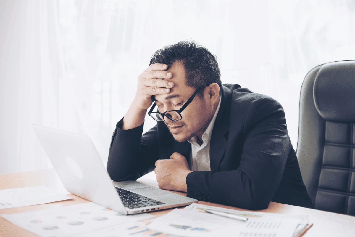 Man sitting in office in front of laptop holding his head with his glasses sliding down his nose